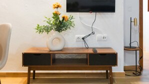 En moderne stue med et fladskærms-tv på væggen, et trækonsolbord med en vase blomster, og en lænestol.