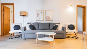 En stue med en grå sofa, to sofaborde, en gulvlampe og to billeder hængende på væggen.