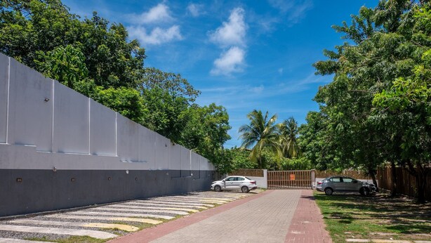 A paved pathway leading to a gated entrance, surrounded by lush greenery and a clear blue sky. - Condominium on the Coast in Imbassai - SOV (Mata de São João)