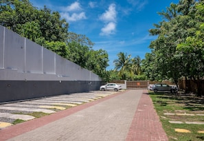 A paved pathway leading to a gated entrance, surrounded by lush greenery and a clear blue sky. - Condominium on the Coast in Imbassai - SOV (Mata de São João)