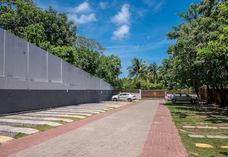 A paved pathway leading to a gated entrance, surrounded by lush greenery and a clear blue sky.