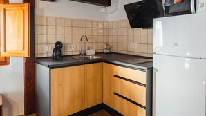 A kitchen with wooden cabinets, a sink, a black microwave, and a white refrigerator. - Quality Homes Granada - QH Correo Viejo 08 (Granada)