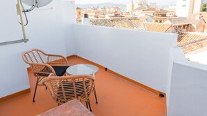 A balcony with wicker chairs and a small table, overlooking a cityscape with terracotta rooftops. - Quality Homes Granada - QH Correo Viejo 08 (Granada)