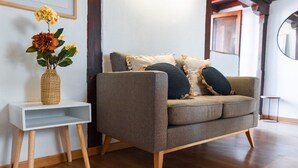 A modern living room with a grey sofa, wooden legs, and a white side table with a woven basket. - Quality Homes Granada - QH Correo Viejo 08 (Granada)