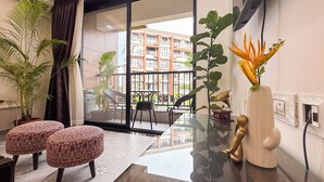 A modern living room with a glass door leading to a balcony, a dining area with a table and chairs, and a variety of potted plants. - Luxury Garden-View 1BHK I Near Candolim Beach I Free Parking I Fast Wifi (Candolim)