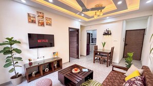 A modern living room with a flat-screen TV, a ceiling fan, and a dining area with a table and chairs. - Luxury Garden-View 1BHK I Near Candolim Beach I Free Parking I Fast Wifi (Candolim)