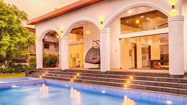 A hotel with a swimming pool, a covered outdoor seating area, and a two-story structure with large windows. - Luxury Garden-View 1BHK I Near Candolim Beach I Free Parking I Fast Wifi (Candolim)