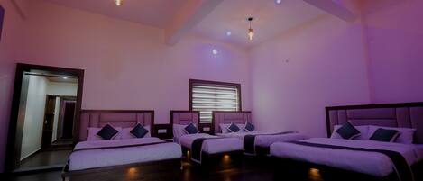 A hotel room with three beds, wooden flooring, and a large mirror.