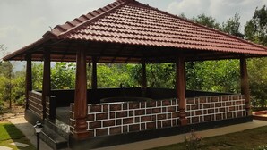A gazebo with a tiled roof and brick walls, surrounded by a well-maintained garden with a pathway. - Mountain Peak Resort  (Alur)