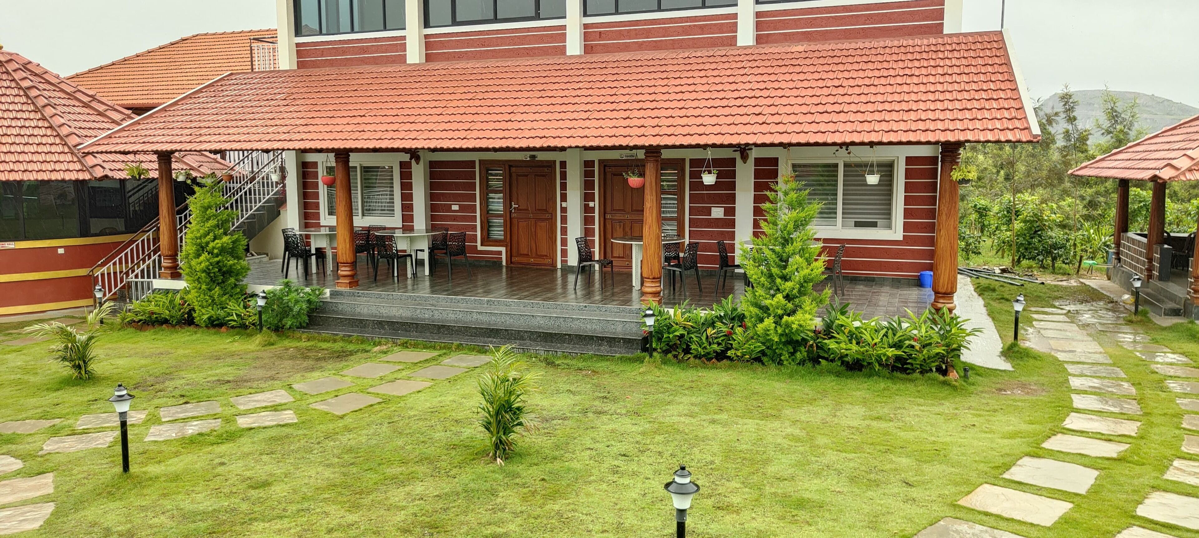Un edificio con techo de tejas rojas, un porche cubierto con asientos al aire libre y un jardín bien cuidado con senderos de piedra.