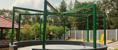 Une aire de jeux comprenant une structure d’escalade circulaire, un toboggan et un petit espace aménagé en scène.