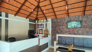 A reception area with a wooden reception desk, a sofa, and a wall with a decorative panel. - Mountain Peak Resort  (Alur)