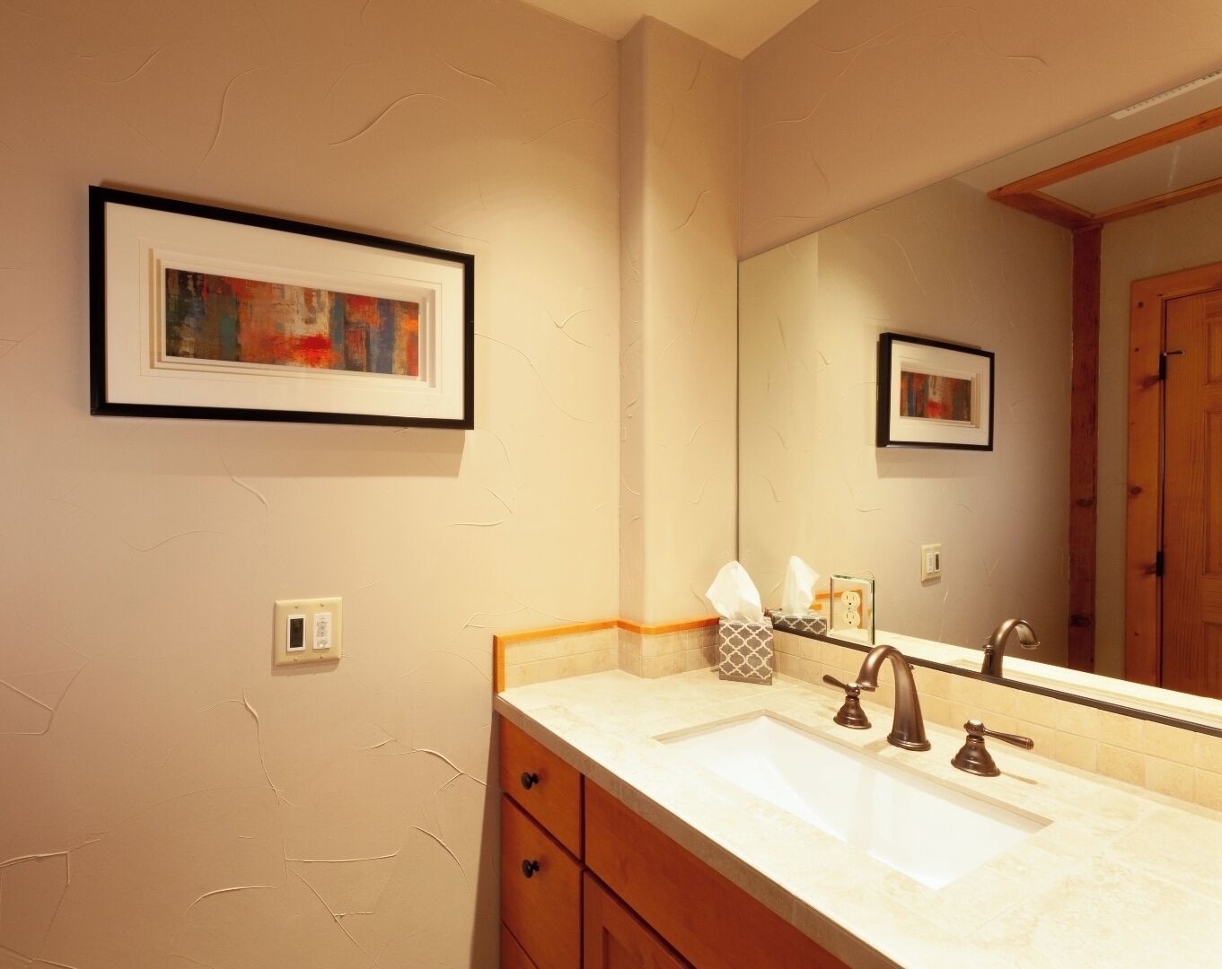 A bathroom with a double sink, wooden cabinets, a framed abstract painting, and a large mirror.