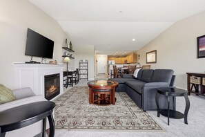 A living room with a fireplace, a television, a sofa, a coffee table, and a dining area in the background. - 1233 - Lighthouse View top floor, steps to beach (Westport)
