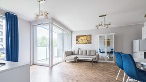 A modern living room with a sofa, a dining table, and chairs. There is a large window and a painting on the wall.