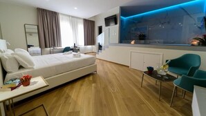 A modern hotel room with a large bed, a desk, a dining area, and a view of the city. - Maqueda Room & Suite (Palermo)