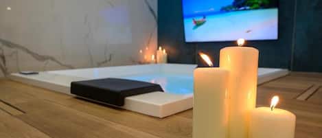 Un área de spa con una camilla de masaje, velas y un televisor que muestra una escena de playa.