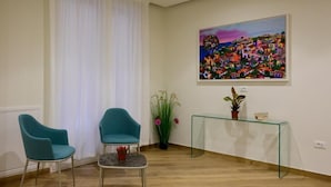 A room with teal chairs, a glass table, a painting, and a potted plant. - Maqueda Room & Suite (Palermo)
