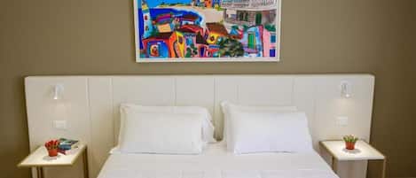 Una habitación de hotel con una cama grande, dos mesitas de noche y un cuadro de un pueblo costero en la pared.
