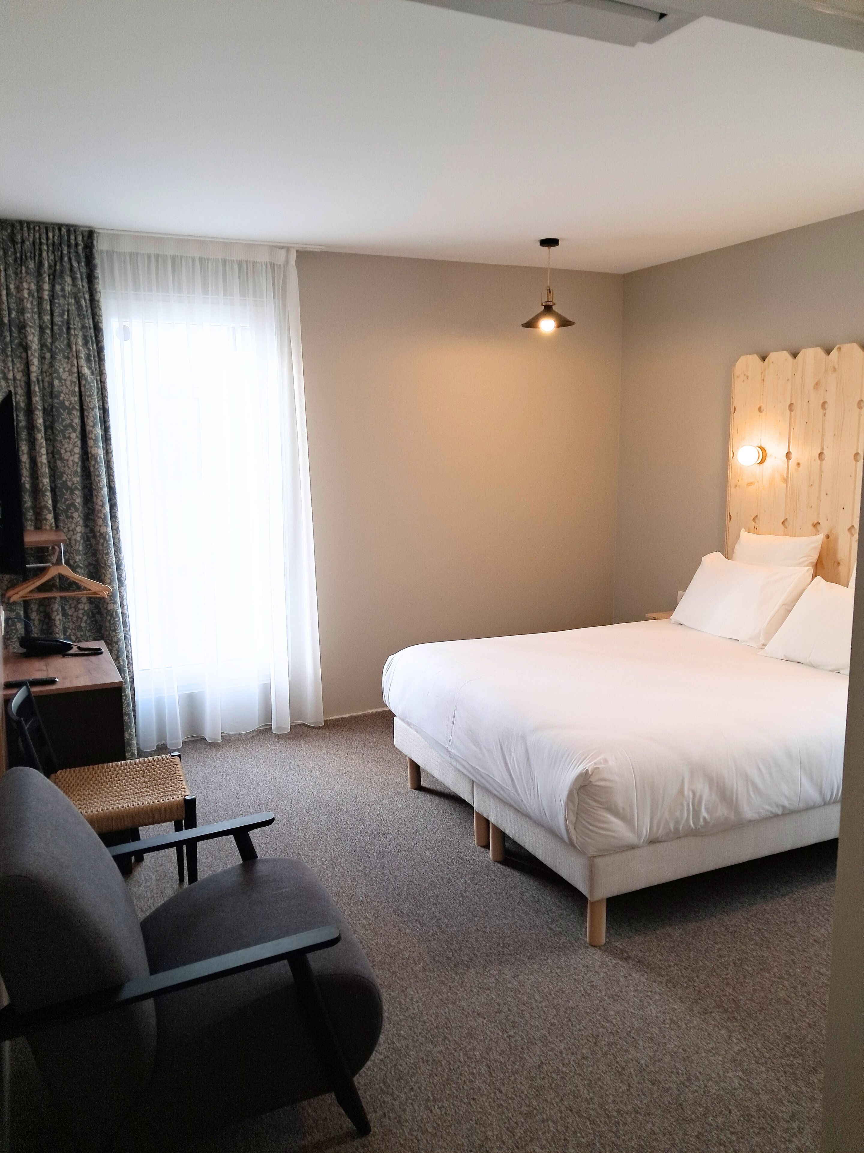 Un dormitorio con una cama, un escritorio, una silla, un televisor y una ventana con cortinas.