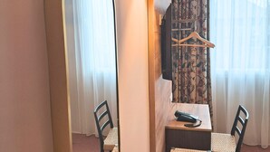Habitación de hotel con comedor, que incluye una mesa, sillas, un espejo grande, una lámpara colgante y un televisor fijado a la pared.
