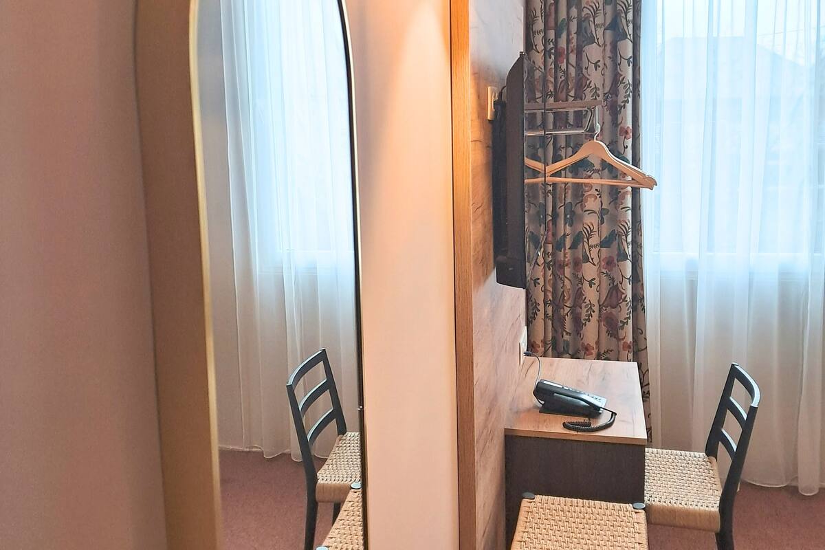 A hotel room with a dining area featuring a table and chairs, a large mirror, a hanging light fixture, and a television mounted on the wall.