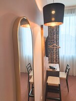 Quarto de hotel com área de jantar, incluindo mesa, cadeiras, um espelho grande, luminária pendente e televisão fixada na parede.