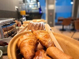 Buffet de café da manhã com croissants e pão, uma torradeira e uma máquina de café.