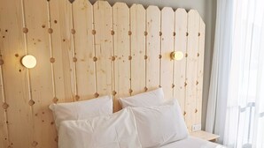 Una cama bien tendida con sábanas blancas en una habitación con cabecera de madera y una lámpara colgante.