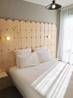 Cama bem arrumada com roupa de cama branca em quarto com cabeceira de madeira e luminária pendente.