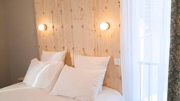 Ein Schlafzimmer mit einem Holz-Kopfteil, zwei Nachttischlampen, einem Bett mit weißen Leinen und einem Fenster mit durchsichtigen Vorhängen.