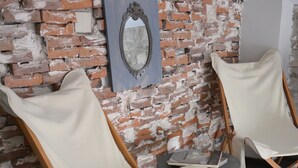 Two white leather chairs with wooden frames against a brick wall, a small table with books, and a decorative mirror. - 8 Design Urla (Urla)