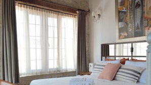 A bedroom with a large bed, a wooden bench, a chair, and a stone wall. - 8 Design Urla (Urla)