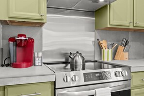 Una cocina moderna con electrodomésticos de acero inoxidable, incluyendo una cafetera, hervidor y estufa.