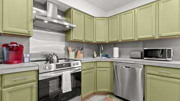 A modern kitchen with green cabinets, stainless steel appliances, and a red coffee maker.