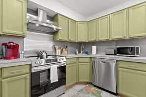 A modern kitchen with green cabinets, stainless steel appliances, and a red coffee maker.