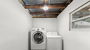 A laundry room with a washing machine and dryer, wooden ceiling beams, and a window.