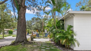 A pathway leading to a small building with outdoor seating, surrounded by greenery and palm trees.