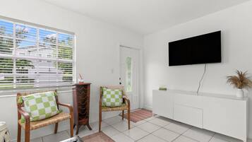 A living room with two wicker chairs, a television mounted on the wall, and a window with blinds.