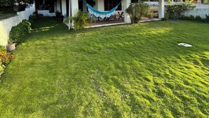 A two-story house with a red-tiled roof and a covered porch. There is a hammock hanging on the porch. The property has a well-maintained lawn and a white fence surrounding it. - House in Vila Lagoinha (Lagoinha)