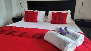 A neatly made bed with red and white bedding, two red pillows, and a white pillow. There are two black nightstands with lamps, and a red blanket on the bed. - Refúgio da Longueira (Longueira)