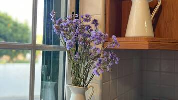 A kitchen with a window, a white pitcher, and a vase with purple flowers.