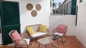 A small patio area with wicker furniture, a glass table, and decorative woven wall hangings. - Refúgio da Longueira (Longueira)