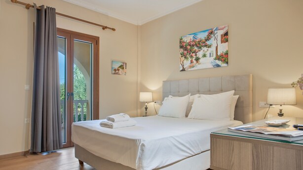 Een hotelkamer met een bed, twee bedlampen, een glazen bijzettafeltje, een schilderij en uitzicht door een glazen deur.