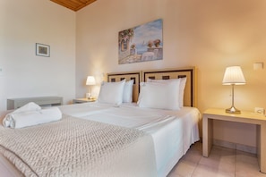 A double bed with white linens, a bedside table with a lamp, a painting on the wall, and a small bedside table with a lamp.