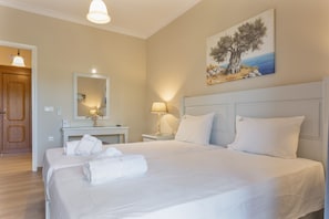 Ein Hotelzimmer mit Bett, Schreibtisch, Lampe, einem Gemälde und einer Tür.