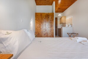 Een slaapkamer met een houten garderobe, een bed met witte lakens, een klein tafeltje en een spiegel boven de wastafel.