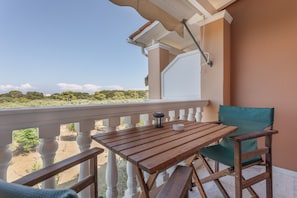 A balcony with a wooden table and a green chair, overlooking a landscape with trees and a clear sky. - Studio Apartment 'Standard  with Sea View 2' with Shared Terrace, Wi-Fi and Air Conditioning (Vasilikos)