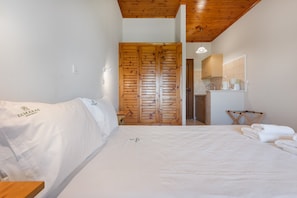 Una camera da letto con un armadio in legno, un letto con lenzuola bianche, un tavolino e uno specchio sopra il lavandino.