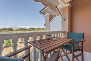 A balcony with a wooden table and a green chair, overlooking a landscape with trees and a clear sky.